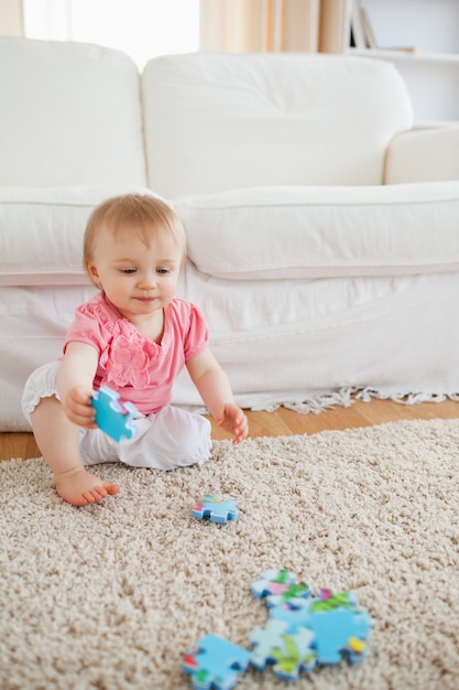 Lovely blond baby playing with puzzle pieces while sitting on a carpet