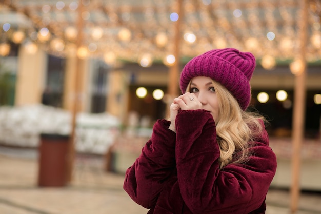 Lovely blonde woman warm her hands on the background of garland at the street in Kyiv