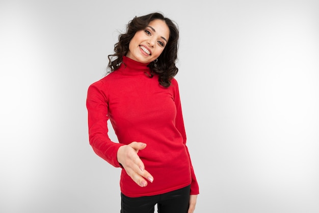 Lovely brunette girl in a red tight-fitting sweater holds out a helping hand on a white background with copy space.