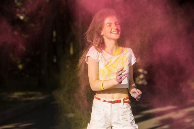 Photo lovely brunette model having fun in a cloud of yellow and pink dry paint at holi festival