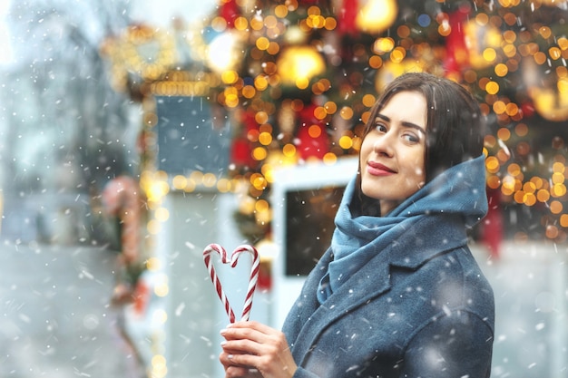 Lovely brunette woman holding candies in a heart shape during the snowfall. Space for text