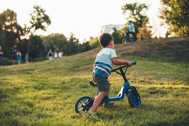 Lovely caucasian boy riding the bike in the park playing on the green grass and looking at the other children