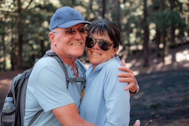 Lovely caucasian senior couple embracing in the woods looking at camera smiling Elderly attractive people enjoying healthy lifestyle hiking in mountain