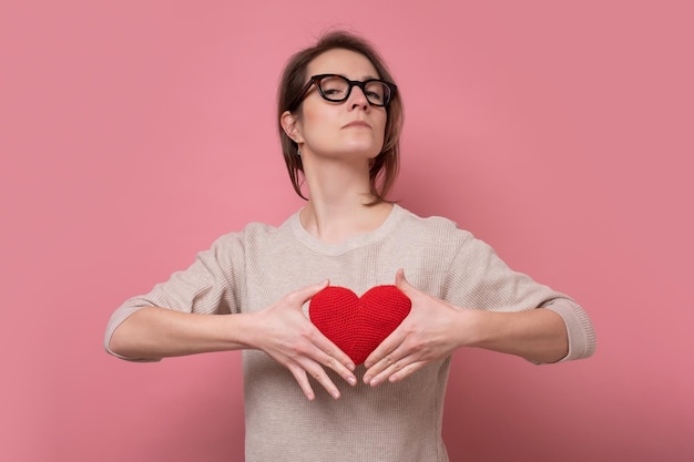 Lovely caucasian woman showing red heart expresses love to you Studio shot on pink wall