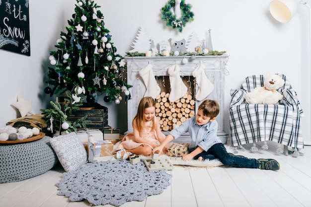 Lovely children playing in room with cristmas tree and fireplace. Winter holidays concept.