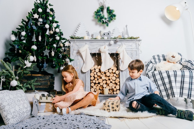 Lovely children playing in room with cristmas tree and fireplace. Winter holidays concept.