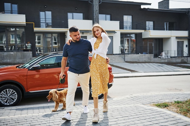 Lovely couple have a walk together with dog outdoors near the car.