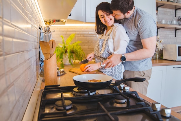 Lovely couple hugging on the kitchen while cooking breakfast