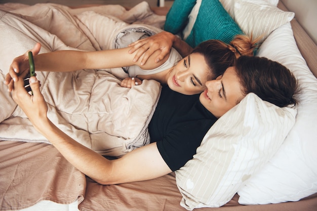 Lovely couple lying in bed and smile while doing a selfie using a mobile phone