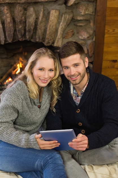 Lovely couple using tablet PC in front of lit fireplace