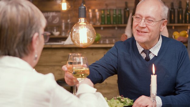 Lovely elderly couple making toast and clinking glasses. Eating in restaurant. Man and woman in their sixties.