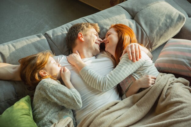 Lovely. Family spending nice time together at home, looks happy and cheerful. Mom, dad and daughter having fun, lying down the sofa. Togetherness, home comfort, love, relations concept.