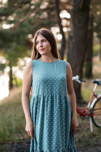 Lovely girl in summer dress on forest road with bicycle