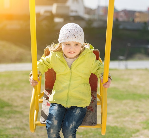 Lovely little girl in yellow coat riding on a swing