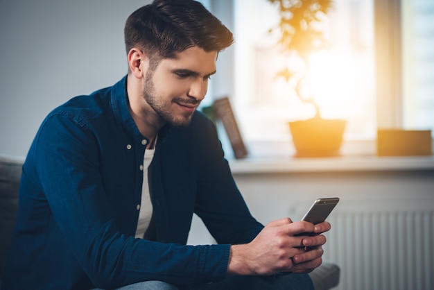 Lovely message from her. Side view of handsome young man using his smartphone with smile 