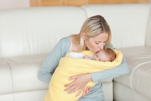 Lovely mother kissing her baby which is wrapped into a cover