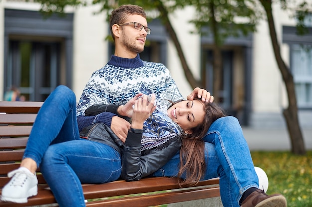 Lovely portrait of a young couple. They are sitting on the bench, embracing and kissing.