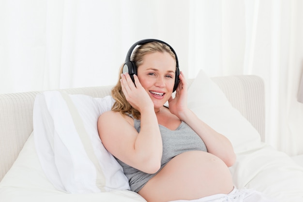 Lovely pregnant woman listening to music on her bed