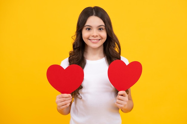 Lovely romantic teenage girl hold red heart symbol of love for valentines day isolated on yellow background Happy teenager positive and smiling emotions of teen girl