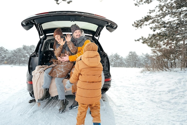 Lovely smiling couple sitting in car trunk in winter forest