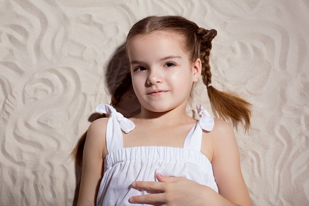 Lovely smiling girl lies on white sand. 