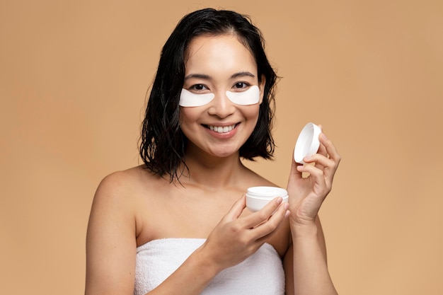 Lovely woman applies beauty patches under eyes and holds jar of cream