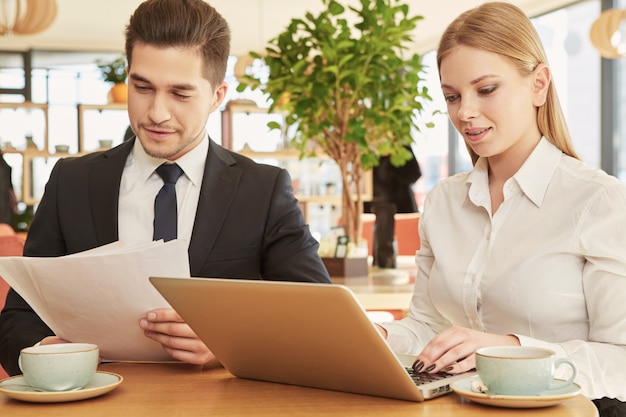 Lovely young business woman typing on her laptop during business  meeting with male colleague