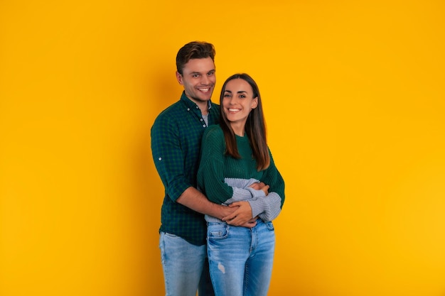 Lovely young couple in love is celebrating ValentineÃ¢ÂÂs Day wearing casual clothes, hugging each other and laughing together while they isolated on yellow background