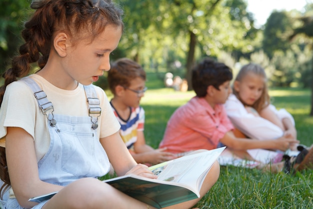 Lovely young girl reading a book outdoors at the park on a warm summer day