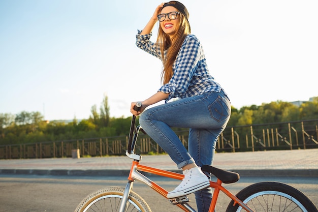 Photo lovely young woman in a hat riding a bicycle on city background in the sunlight outdoor active people