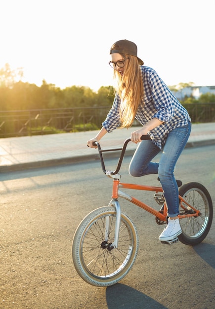 Lovely young woman in a hat riding a bicycle on city background in the sunlight outdoor Active people