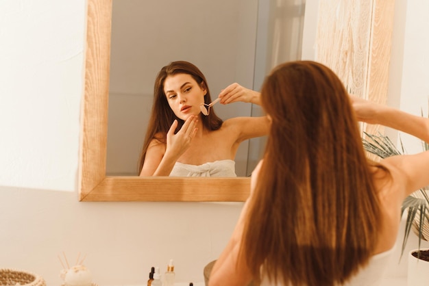 Lovely young woman massages the contour of her face with a jade roller Beauty and antiaging procedure for skin care