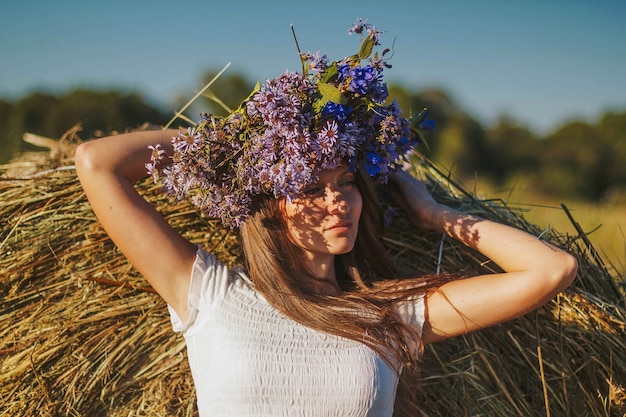 Lovely young woman in white dress by the haystack.  Female portrait in field in countryside.