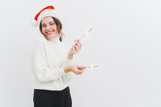 Lovely young woman in white sweater holds sparklers and laughs smiles with a wide smile