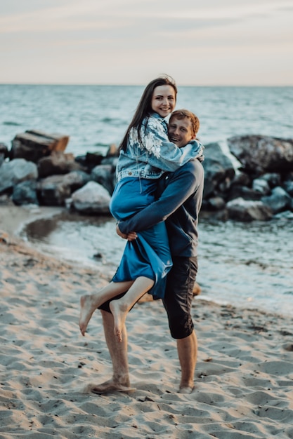 Lovers are laughing on the beach. The guy carries the girl in his arms.