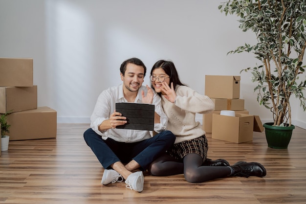 Lovers are sitting on floor in newly bought apartment elegantly dressed man is holding tablet couple