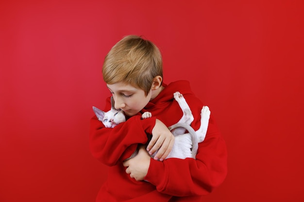 Loving boy in a red suit holds a little kitten in his arms hugs him and kisses him