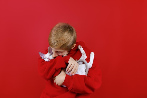 Loving boy in a red suit holds a little kitten in his arms hugs him and kisses him