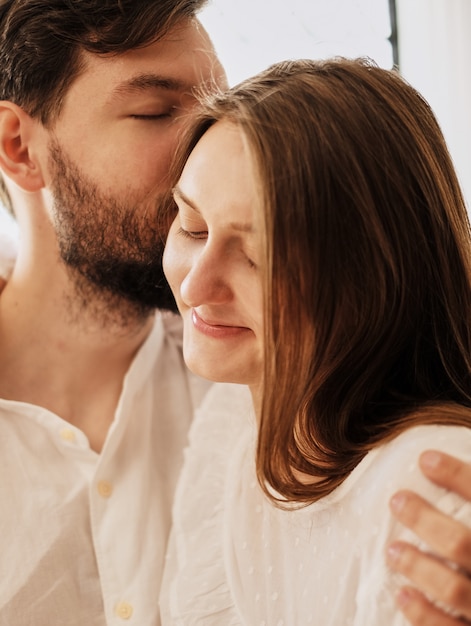 loving boyfriend kisses his girlfriend's ear. hugging gently kiss. lovers are dressed in pajamas