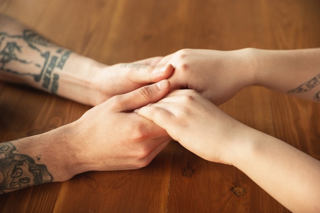 Loving caucasian couple holding hands close-up on wooden wall. Romantic, love, relation, tender touching. Supporting and helping hand, family, warm. Togetherness, feeling and emotions.