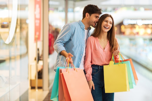 Loving couple carrying shopper bags shopping and flirting in mall