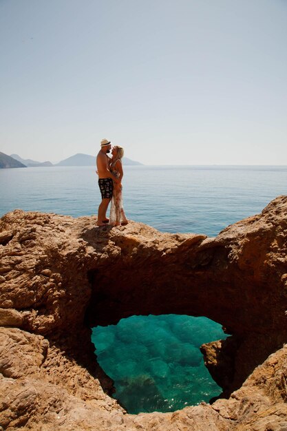 Loving couple enjoying honeymoon on rock with luxury view walking showing emotion on azure sea background