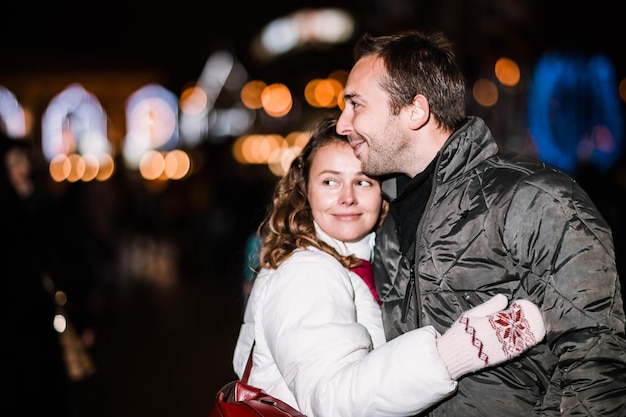 Loving couple in a festive city with New Year's lights in the winter evening. Spouses in winter clot