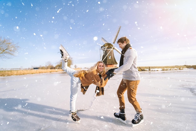 Loving couple having fun on ice in typical dutch landscape with windmill woman and man ice skating