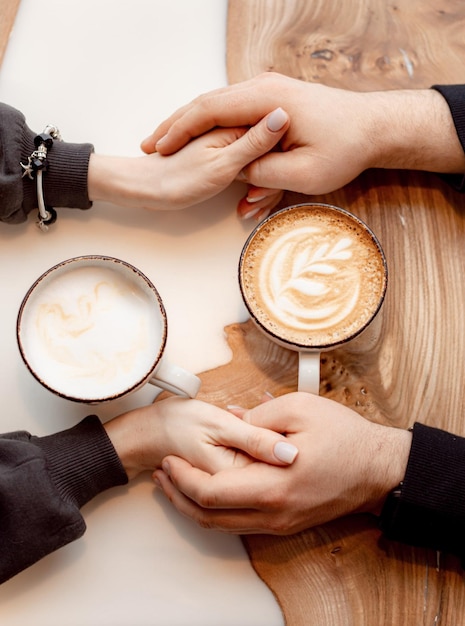 Loving couple holding hands with coffee on a white wooden table