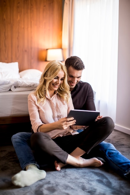 Loving couple sitting on the floor in bedroom and using digital tablet