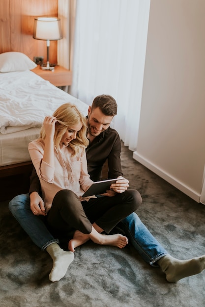 Loving couple sitting on the floor in bedroom and using digital tablet