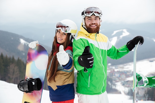 Loving couple snowboarders on the slopes frosty winter day making thumbs up gesture