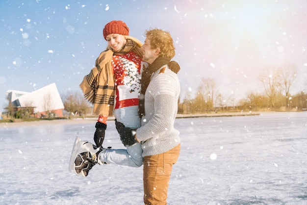 Loving couple in warm sweaters having fun on ice woman and man ice skating outdoors in sunny snowy