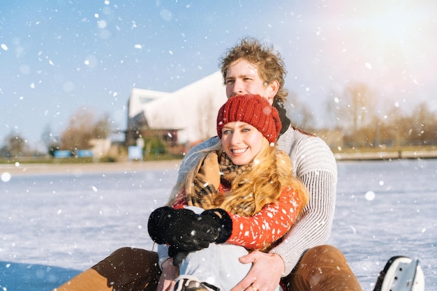 Loving couple in warm sweaters having fun on ice woman and man ice skating outdoors in sunny snowy